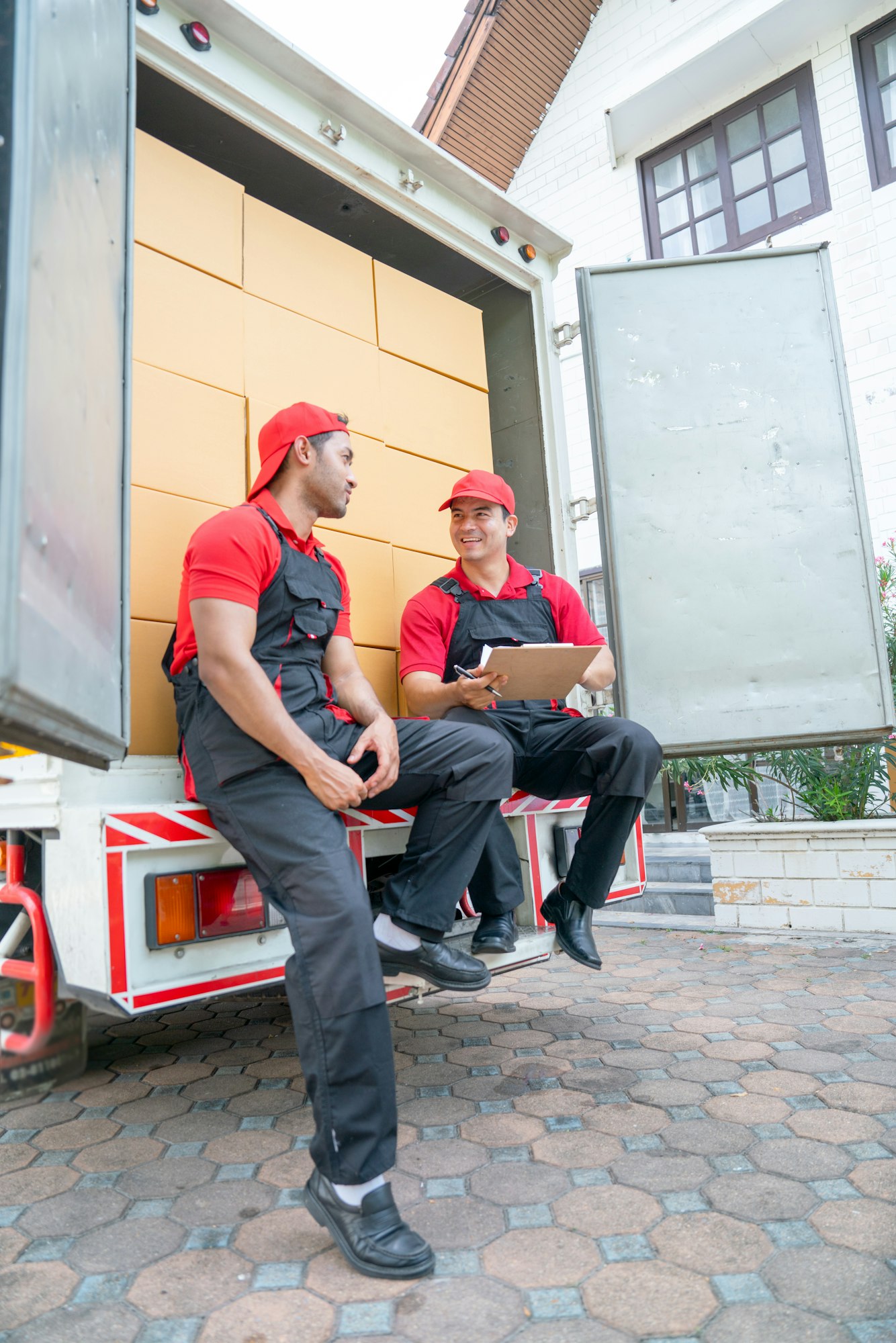 vertical image of two delivery men sit and discuss together on back part of truck during move box